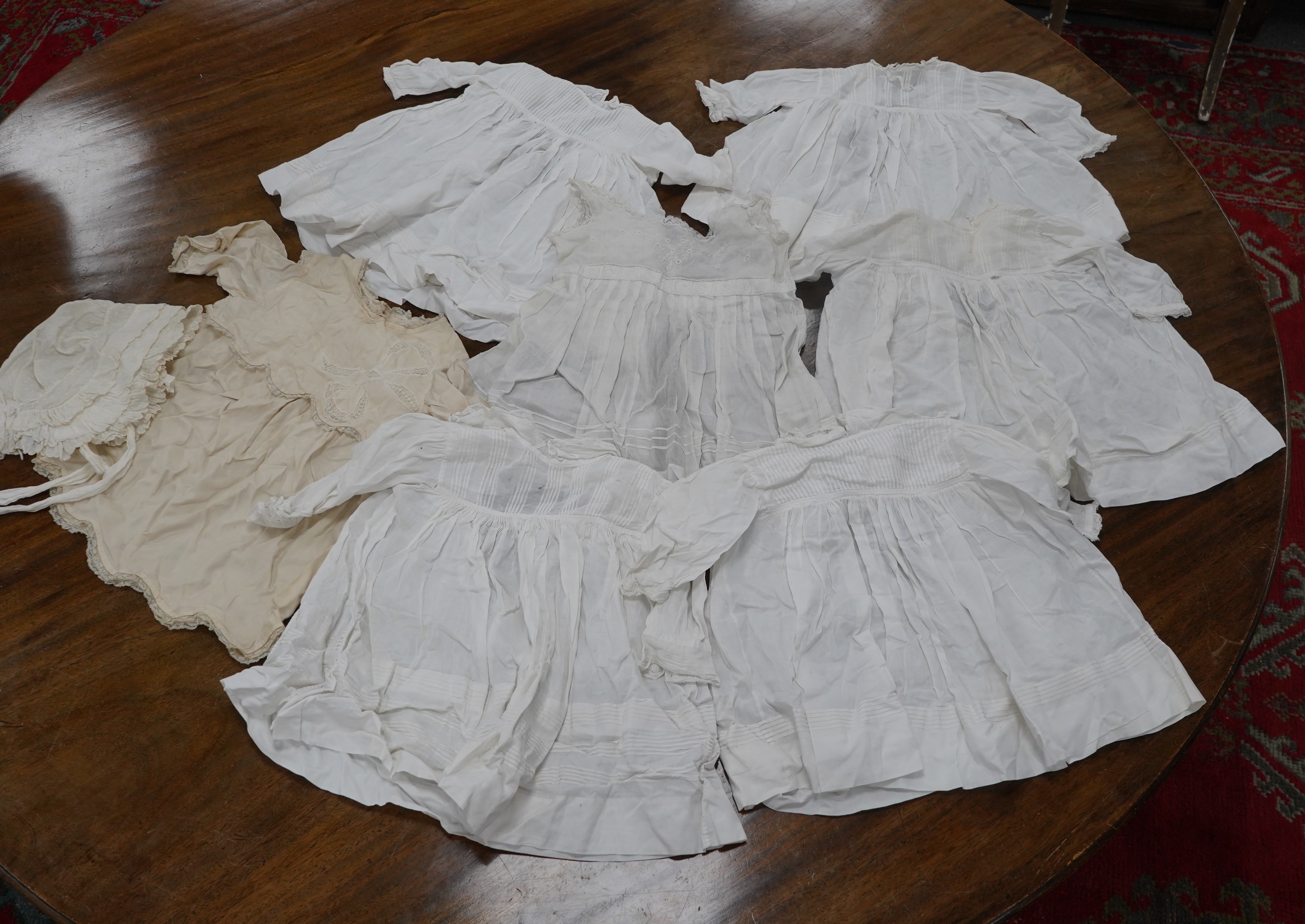 An early 20th century cream silk young girls day dress, together with six similar sized cotton and fine lawn day dresses and a bonnet, all dresses worked with tucking, feather stitching, some lace edged, the bonnet made